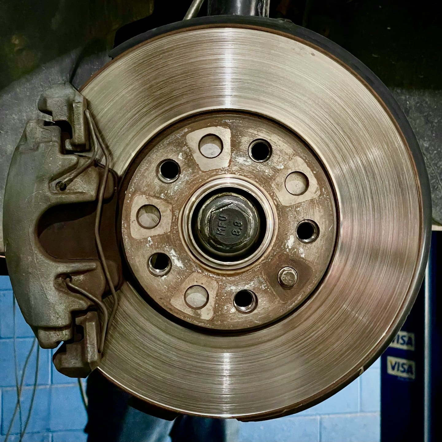 Silver car brake disc and grey caliper with bolt.