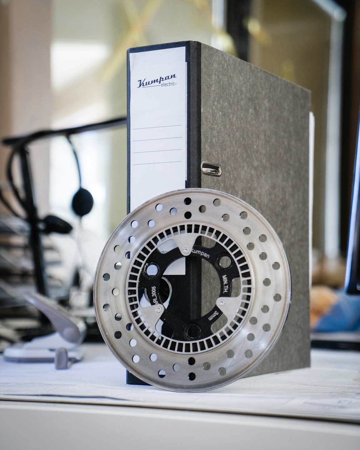 Metal brake disc with holes leaning on a file binder.
