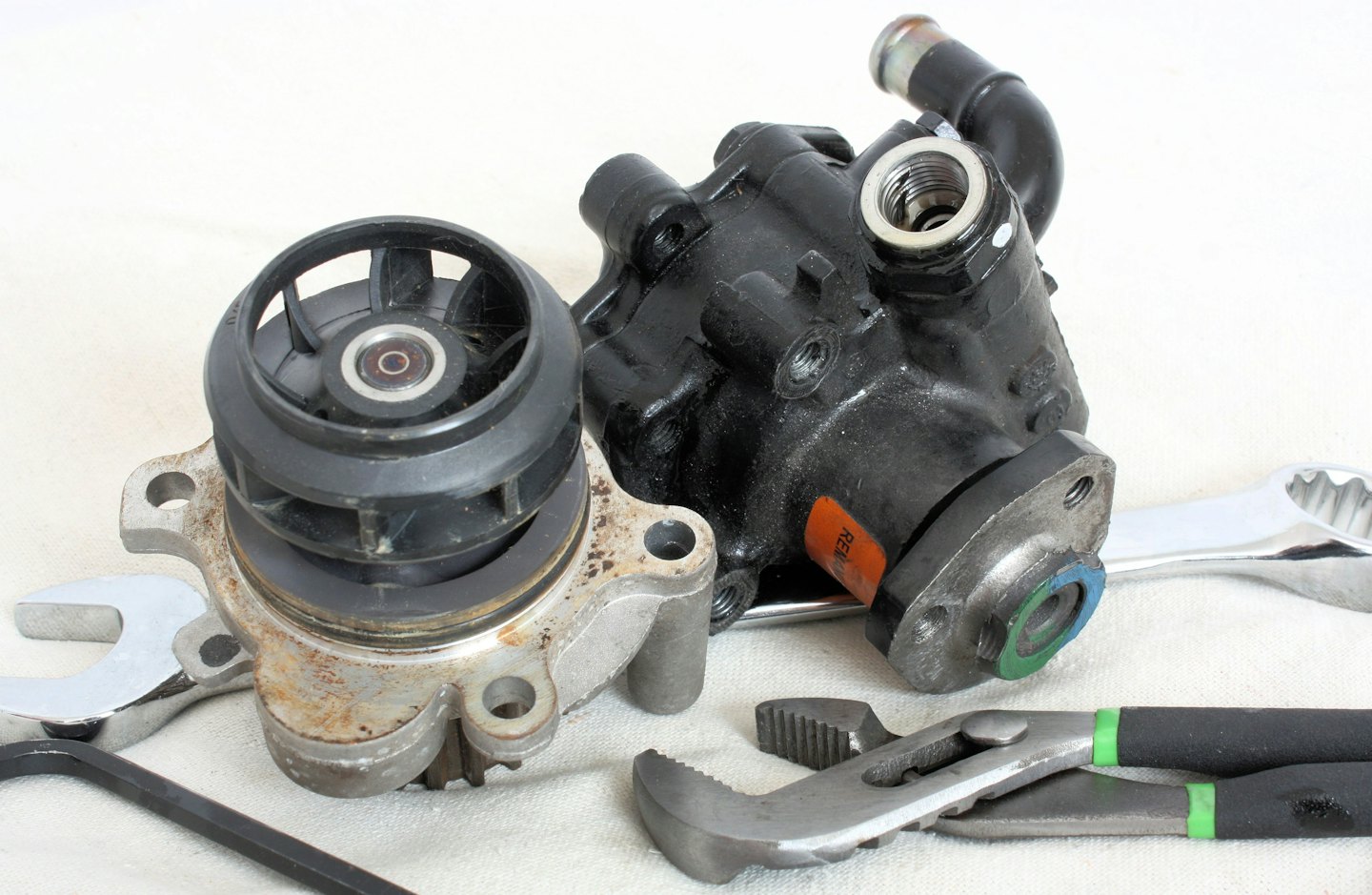 Assorted automotive parts and mechanic tools on a white surface.